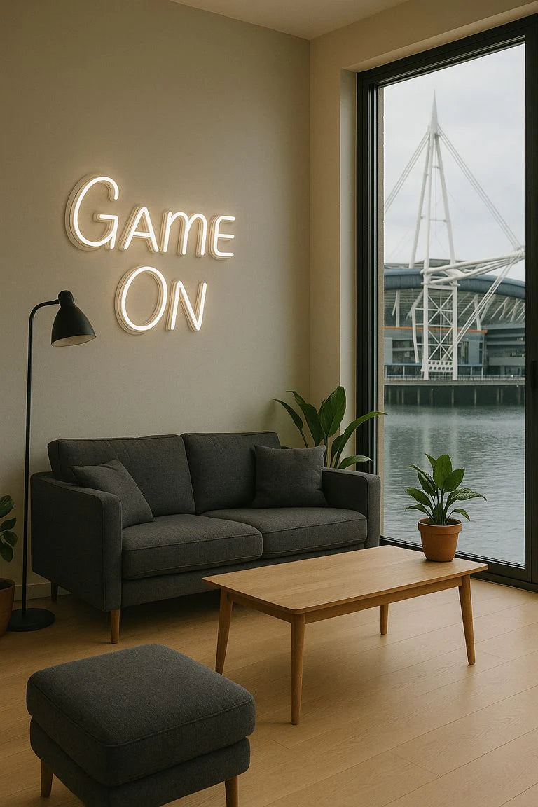 Game On LED neon sign on wall in modern Cardiff apartment living room, with stadium view through window, warm white custom neon decor.