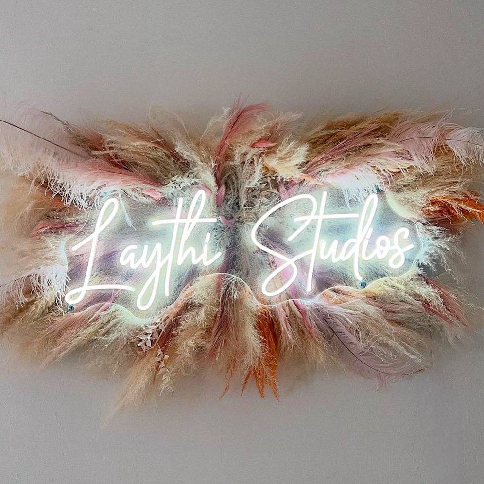 White LED neon Laythi Studios sign displayed against a dried floral arrangement